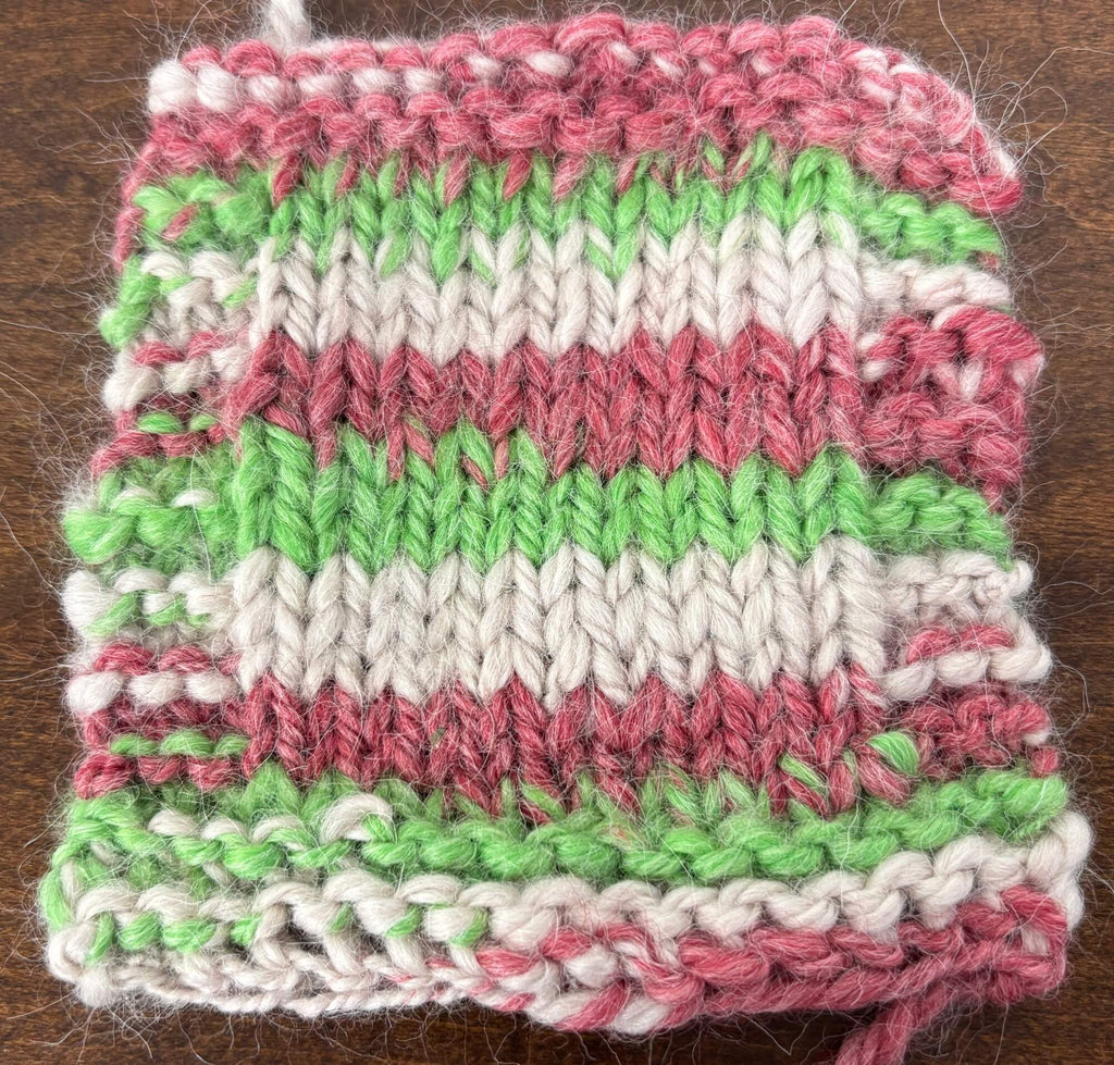 Knitted square with red, green, and white stripes on a wooden surface