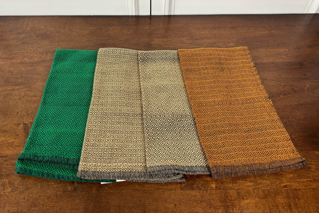 Four folded towels in green, beige, and orange on a wooden surface.