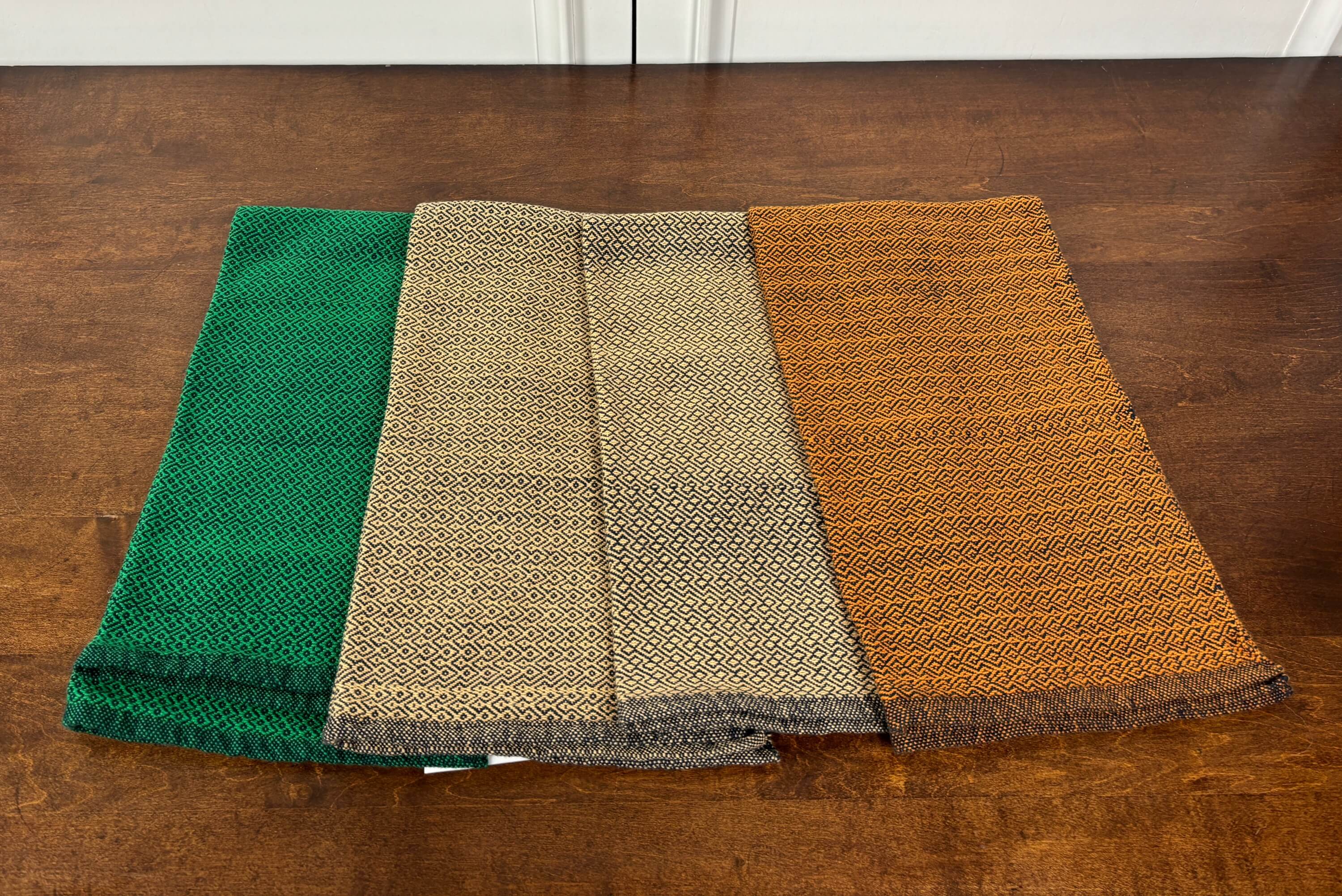 Four folded towels in green, beige, and orange on a wooden surface.