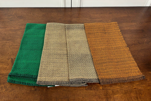 Four folded towels in green, beige, and orange on a wooden surface.