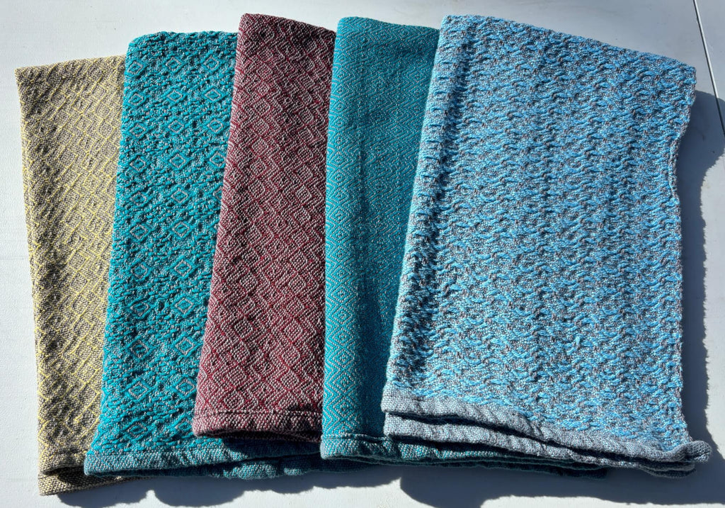 Five textured towels in different colors arranged on a flat surface.