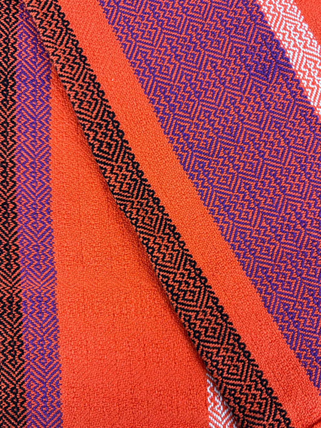 Close-up of fabric with geometric pattern in Orange, purple, and black.