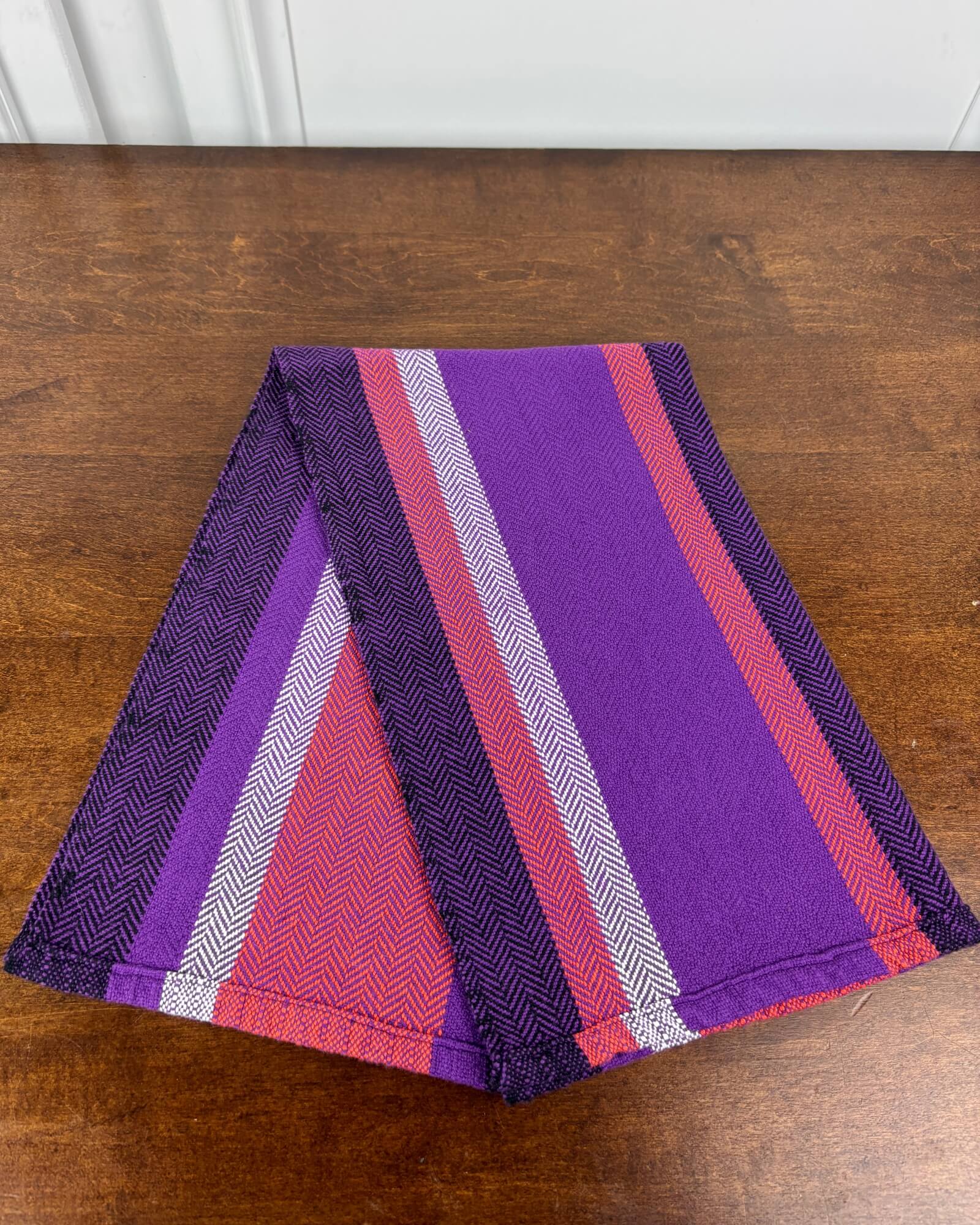 Folded striped towel with purple, Orange, and white pattern on a wooden surface