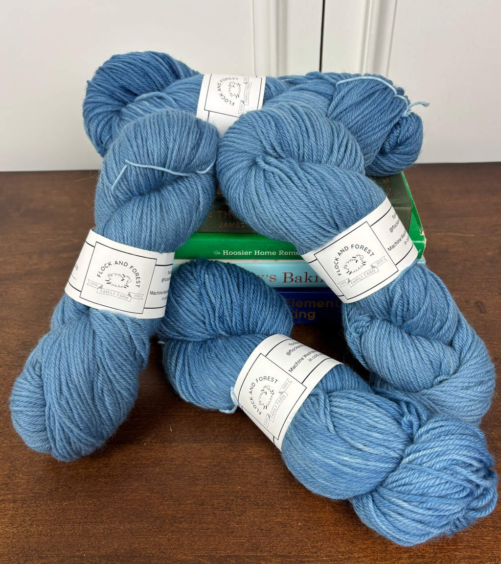 Four skeins of blue yarn on a wooden surface with a white background