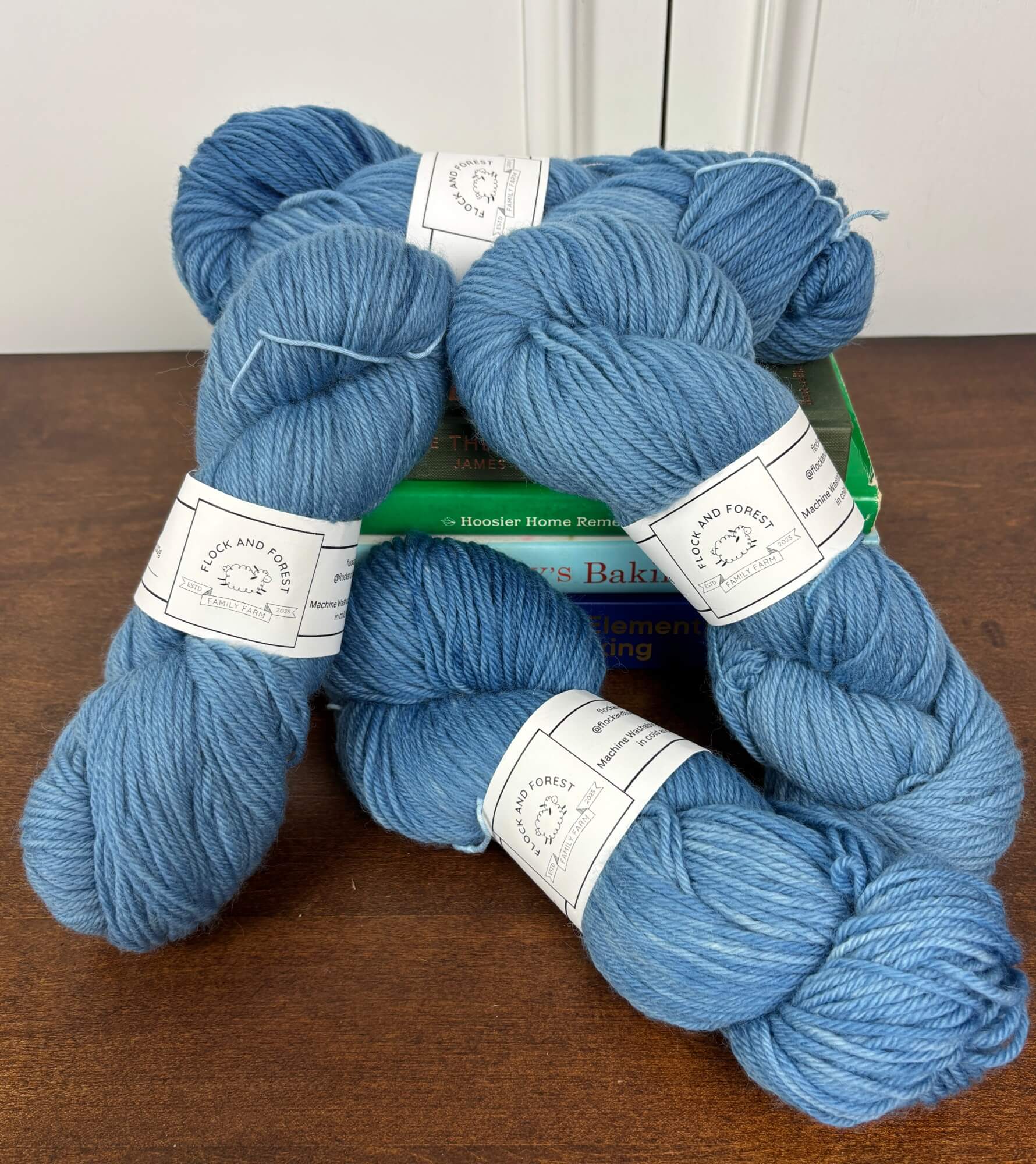 Four skeins of blue yarn on a wooden surface with a white background