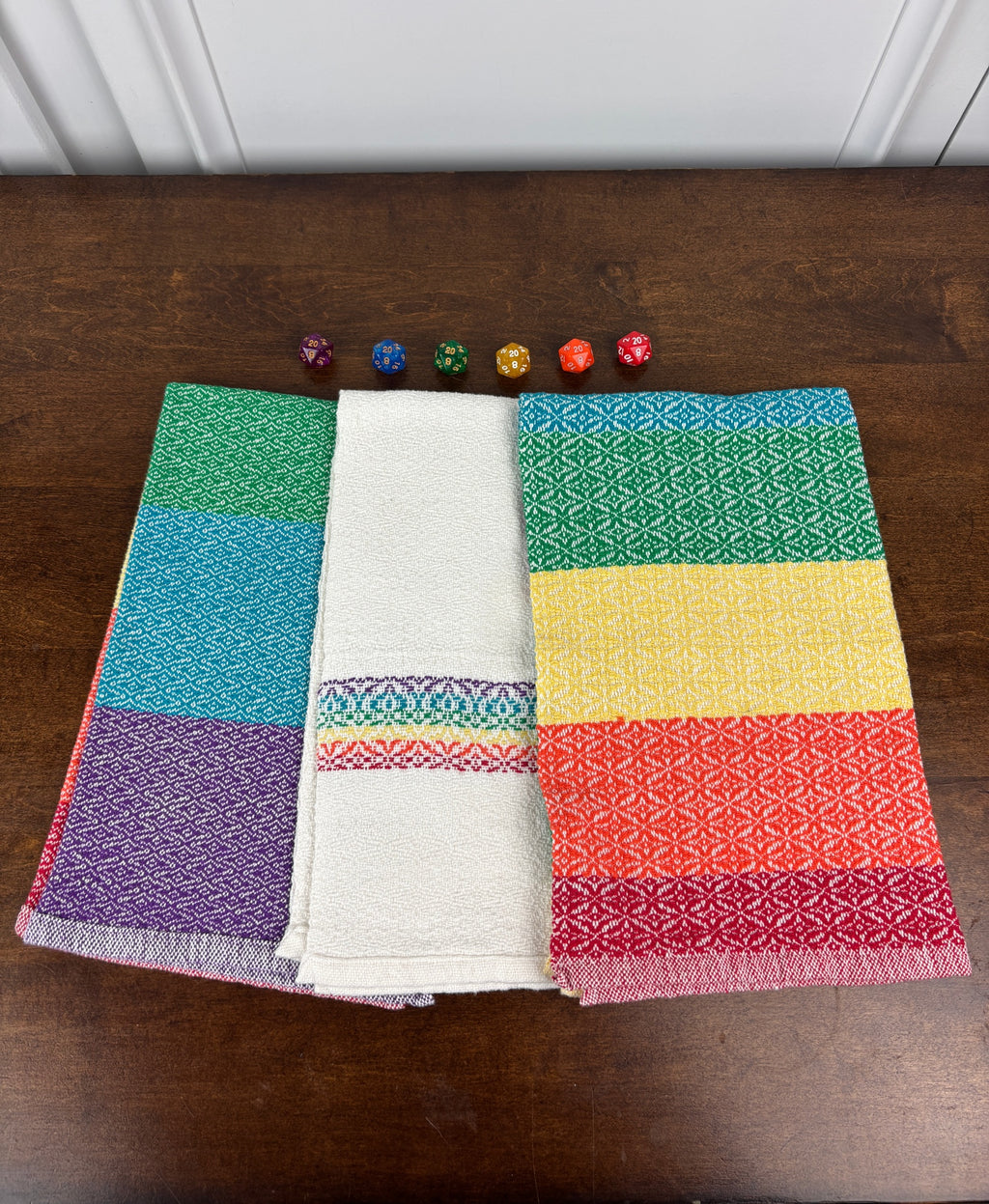 Set of rainbow colored woven towels on a wooden surface with small decorative items.